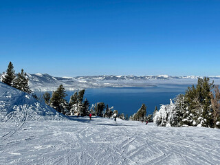 Scenic view of skiers and snowboarders on the slopes of a ski resort on a bluebird winter day, with...