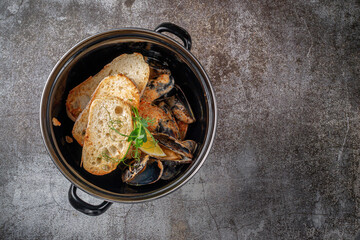 Serving a dish from a restaurant menu. Fried mussels with croutons and lemon in a dark pan against a gray stone table