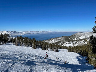 Scenic view of skiers and snowboarders on the slopes of a ski resort on a bluebird winter day, with Lake Tahoe in the background