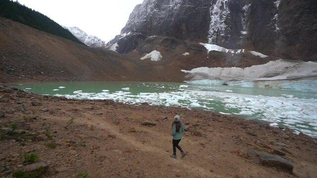 Lonely Woman Walking by Glacial Lake With Icebergs Under Glacier in Canadian Highlands. Mount Edith Cavell, Alberta 60fps