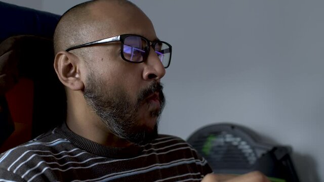 A middle-aged man is having a snack in front t of his computer. He is wearing eyeglasses.
