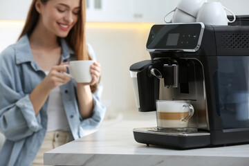 Young woman enjoying fresh aromatic coffee in kitchen, focus on modern machine