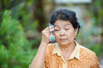 Old Thai woman massages eye sockets because of eye pain after using too much eyes. Health care...