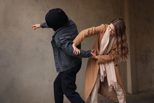 Woman defending herself from attacker near beige wall outdoors