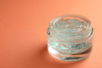 Jar of cosmetic gel on pale orange background, space for text