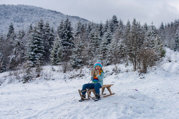 Boy sledding on winter mountain, enjoying a sledge ride in a beautiful snowy winter park. Winter scene with snowy forest.