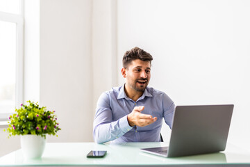 Young businessman in eyewear wearing headphones, holding video call with clients on laptop.