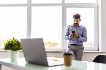 Good business talk. Handsome young man use phone and using computer while working in the office