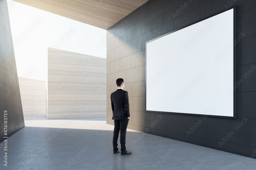 Poster Businessman in abstract concrete tile space interior background with empty white mock up poster and sunlght. Design and abstraction concept.
