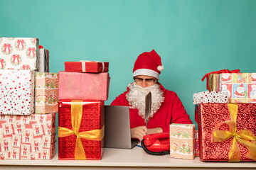Santa Claus wearing hat work in his oficce with presents, preparing for holidays.