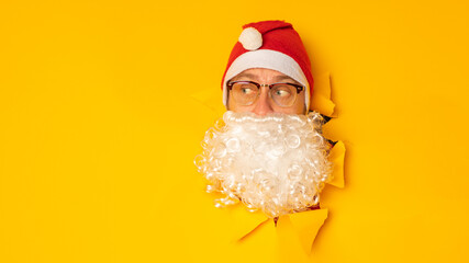 Santa Claus looking through hole in paper. Man in Santa hat. Winter holiday. Christmas celebration. Merry Christmas and Happy New Year.