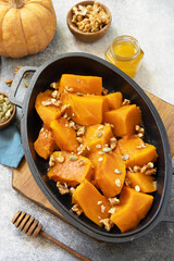 Healthy dessert or vegan lunch. Baked pumpkin. Delicious baked sweet pumpkin with nuts, pumpkin seeds and honey over gray stone background.
