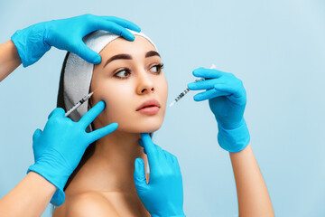 Portrait of a beautiful young woman with hands of cosmetologists in medical gloves lean syringes...