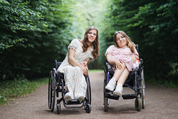Plakat Happy young women with physical disability enjoying summer walk at green park. Female wheelchair users supporting and understanding each other.