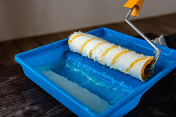 The roller for applying glue to the wallpaper in blue tray.