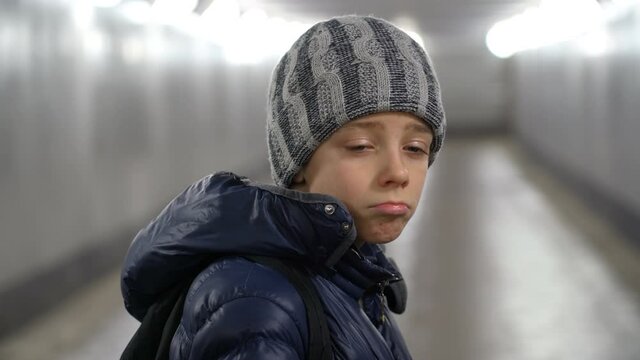 Portrait of alone sad boy in hat and jacket in underground covered walkway in city at winter