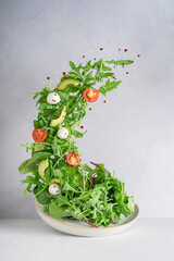 Levitation or flying of vegetarian green salad made of rocket leaf or arugula, sliced cherry...
