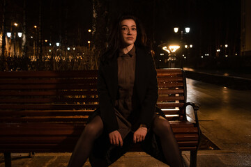 Lonely girl on a bench in the night city park.