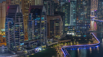 Dubai Marina with several boat and yachts parked in harbor and skyscrapers around canal aerial night timelapse.