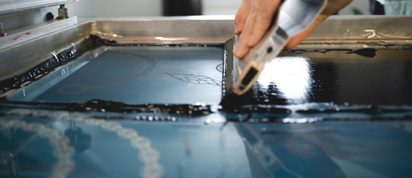 Close up of artisan applying ink on stencils on screen printing machine in workshop 