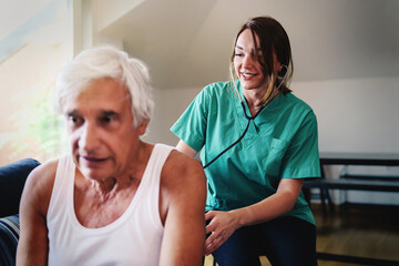 Assisted living - female doctor checking the heartbeat of the elderly patient at home