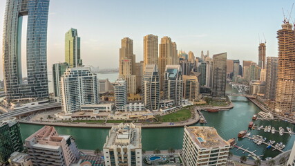 Panoramic view of Dubai Marina with several boat and yachts parked in harbor and skyscrapers around canal aerial day to night timelapse.