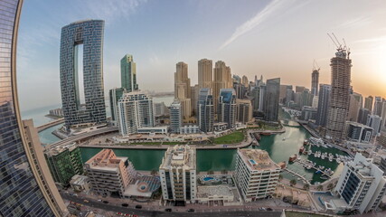 Dubai Marina with several boats and yachts parked in harbor and skyscrapers around canal aerial morning timelapse.