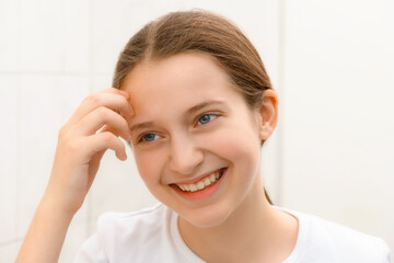 face of a happy teenage girl, she looks at herself in the mirror and touches her face with her hand, good and clean skin is a concept of beauty and health