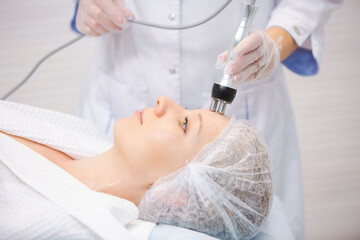 Close up portrait of a beautiful smiling woman relaxing during the RF lifting procedure in a modern beauty salon