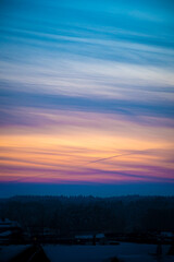 Bright evening sky in Lithuania. Orange and blue cloudscape, dusk illuminating the clouds. Dark forest in the foreground. Selective focus on the details, blurred background.