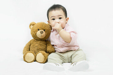 Adorable asian baby boy in pink shirt sucking his finger,sitting and hugging teddy bear.
