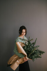 Millennial woman holding big bunch of pine branches wrapped in craft paper, going to make Christmas wreath and festive holiday decorations