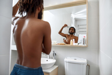 Black man applying deodorant on body in bathroom