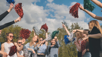 Cheerful girls in the meadow waving multi-colored cheerleading pompoms.