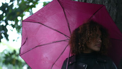 Young black woman holding pink umbrella outside during rainy day