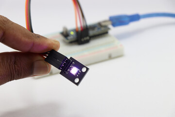 ARGB LED module held in hand connected to micro controller on background, LED module with glowing...