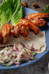 Serving a dish from the restaurant menu. Chicken wings, grilled nuggets with grated carrots and herbs on a plate against a gray stone table, delicious kebab