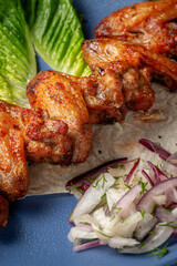 Serving a dish from the restaurant menu. Chicken wings, grilled nuggets with grated carrots and herbs on a plate against a gray stone table, delicious kebab