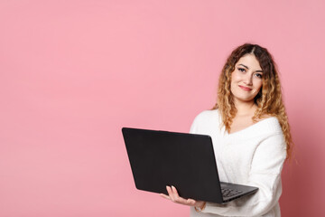 Woman standing isolated on a pink background using a laptop computer.