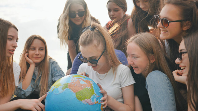 A group of cheerful girls is exploring the globe of the world in the meadow. - Powered by Adobe