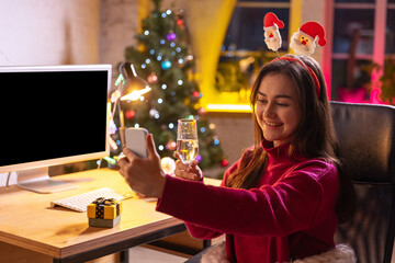 Cute happy young girl talking with friends by means of video call and celebrates winter holidays at home