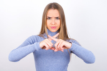 Young caucasian girl wearing blue turtleneck over white background has rejection angry expression...