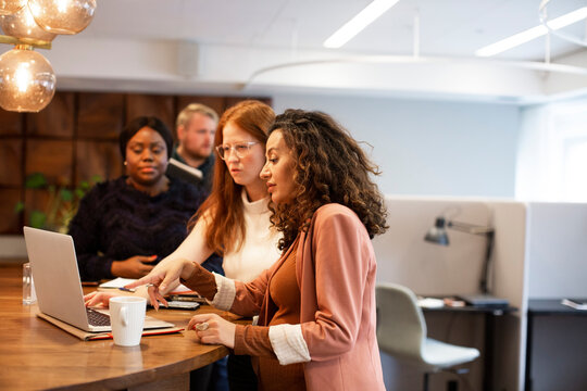 Pregnant businesswoman discussing with colleagues over laptop at office