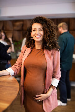 Portrait of pregnant female boss standing by desk in office