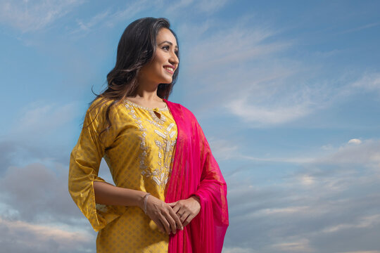 Happy woman in yellow salwar standing under the blue sky