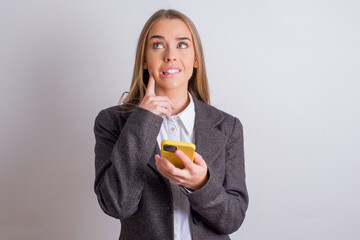 Image of a thinking dreaming Young business woman wearing jacket over white background using mobile...