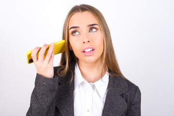 Smiling Young business woman wearing jacket over white background listening a voice message from her smartphone. Communication and technology concept.