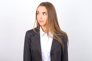Young business woman wearing jacket over white background stares aside with wondered expression has...