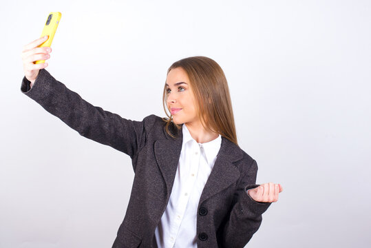 Portrait of a Young business woman wearing jacket over white background taking a selfie to send it to friends and followers or post it on his social media.