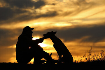 Silhouette of a man and a Malinois dog on a sunset background